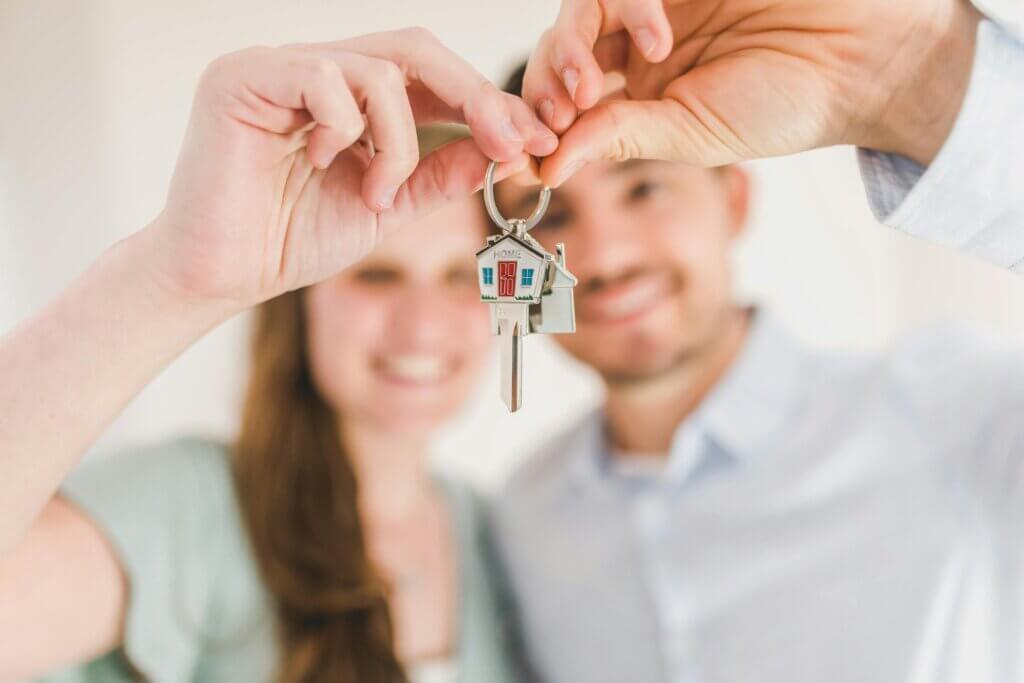 Ein Pärchen hält einen Haustürschlüssel gemeinsam vor sich in die Luft.